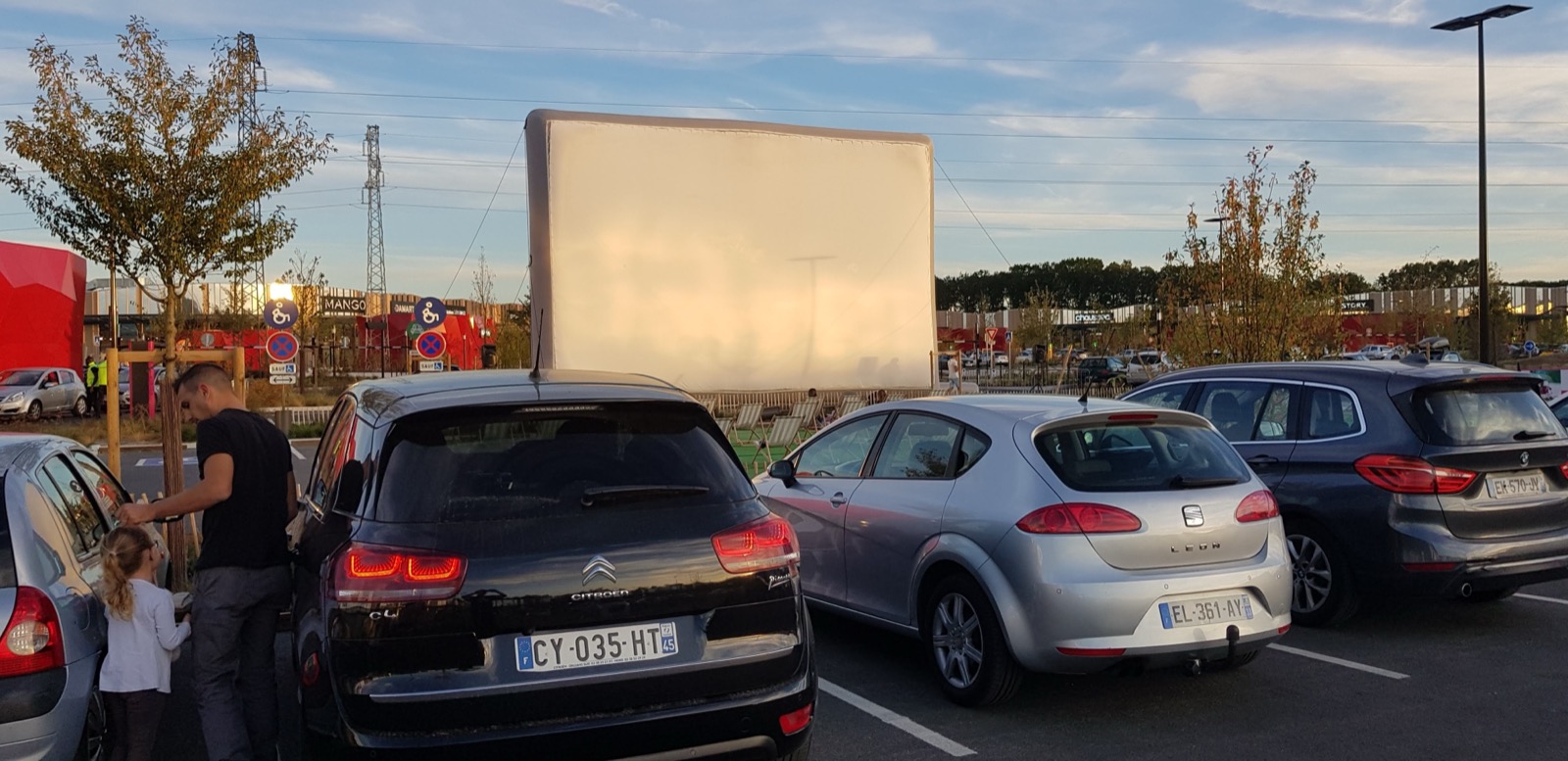 Pantalla de cine hinchable gigante «Hallucine» instalada al aire libre, con coches aparcados cerca